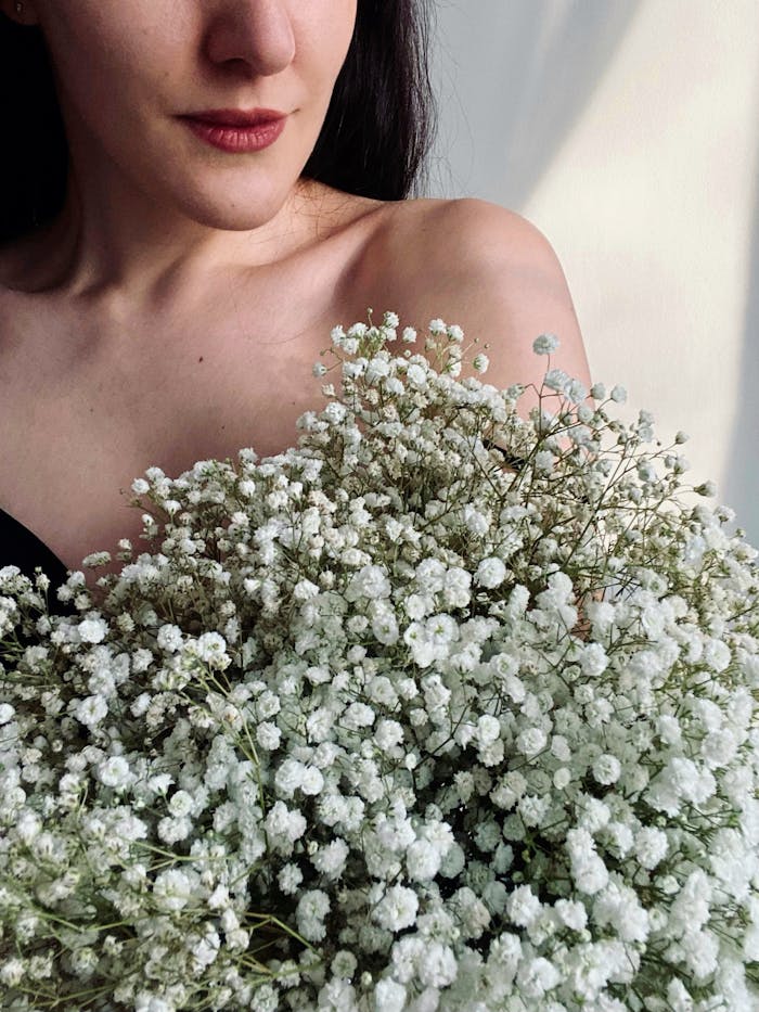 A woman gently holding a bouquet of white babys breath flowers, bathed in soft, natural light.